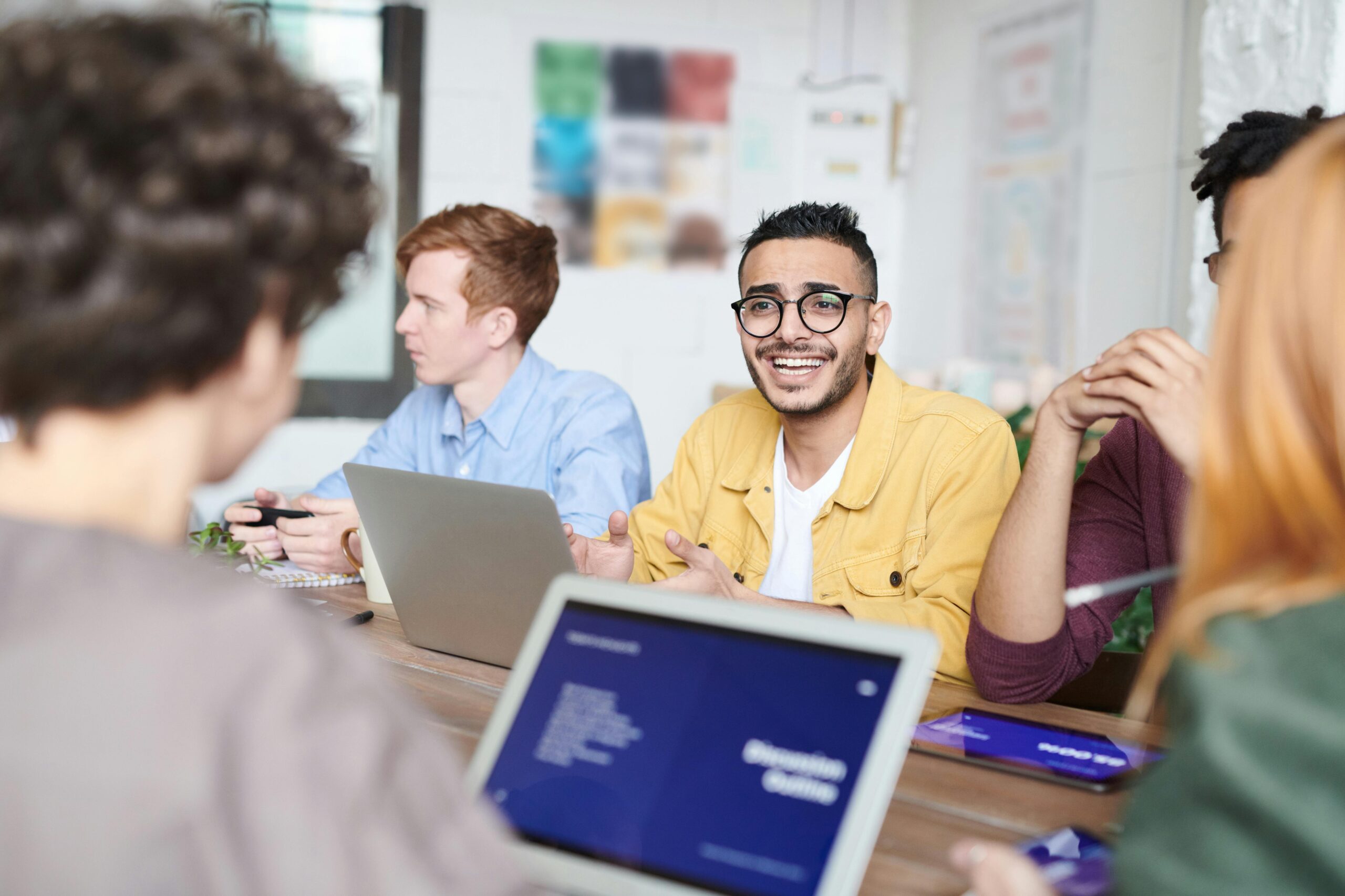 A diverse group discussing a project with laptops in a modern office meeting room.